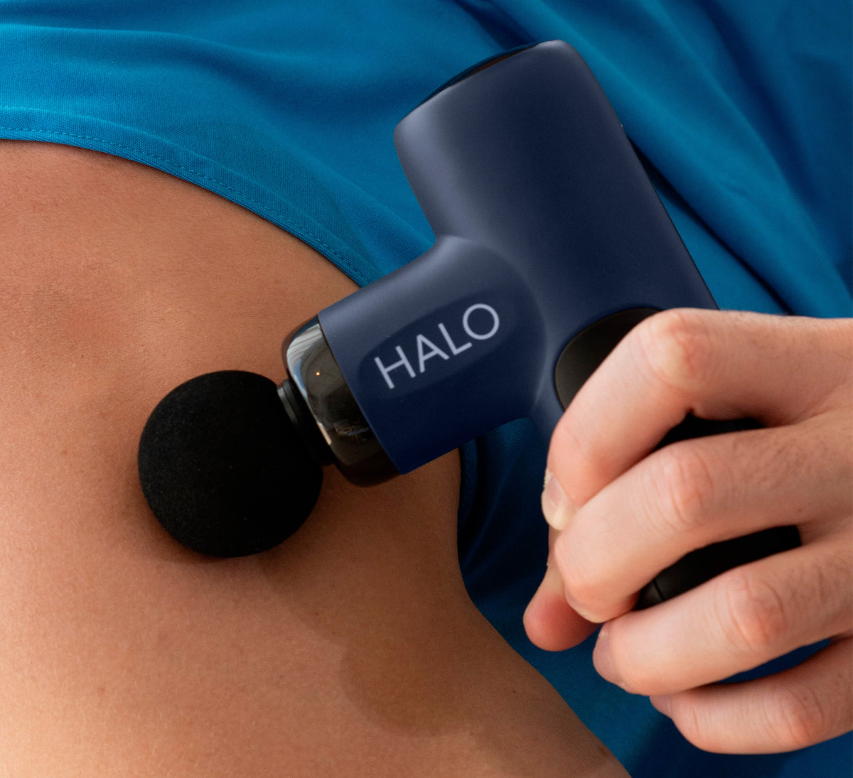 Hand holding Halo Compact Percussion Massager against shoulder for targeted muscle recovery and sore joint relief.