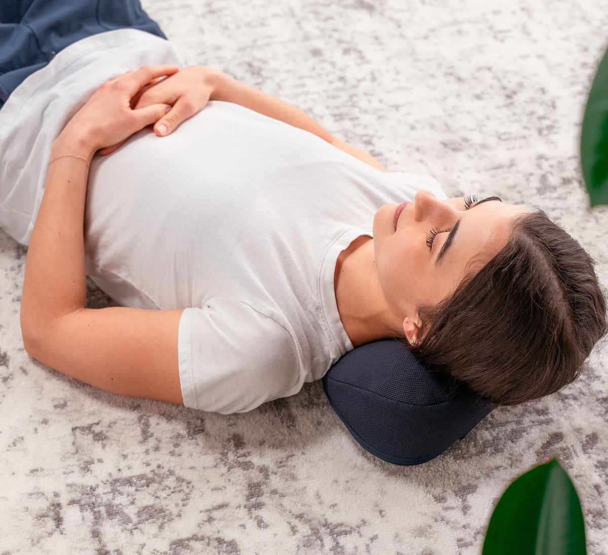 Woman resting on back with dark blue neck and head support pillow during floor relaxation | Halo Neck Stretch Pillow